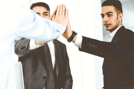 Business people group showing teamwork, joining hands and giving five to each other in modern...