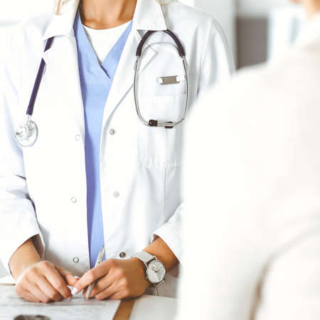 Unknown woman-doctor sitting and communicating with female patient. Physician checks medical history...
