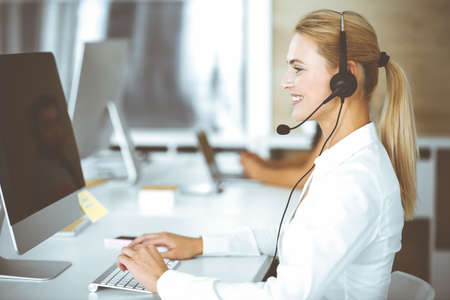 Blonde business woman using headset for communication and consulting people at customer service...