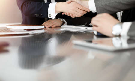 Unknown businessman shaking hands with his colleague or partner above the desk in sunny office,...