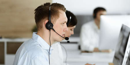 Group of diverse operators at work in call center. Businessman sitting n headset at customer service...