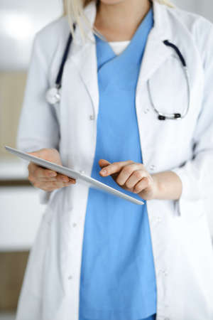 Unknown woman-doctor standing in clinic and using tablet pc, close-up. Data and best service in...