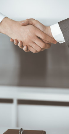 Unknown businessman shaking hands with his colleague or partner while standing straight in modern office, close-up. Business people group at meetingの写真素材
