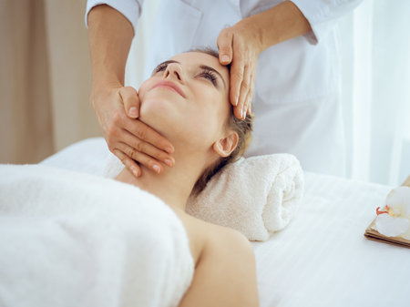 Young and blonde woman enjoying facial massage in spa salon. Beauty conceptの写真素材