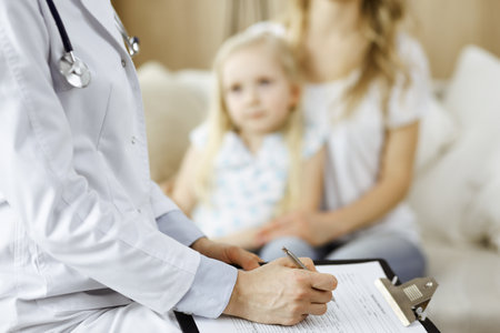 Doctor and patient. Pediatrician using clipboard while examining little girl with her mother at home. Happy cute caucasian child at medical exam. Medicine conceptの写真素材