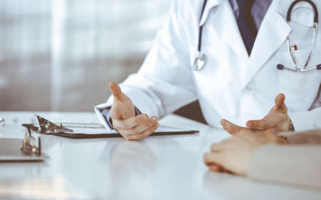 Unknown male doctor and patient woman discussing something while sitting in clinic and using clipboard. Best medical service in hospital, medicine, pandemic stopの写真素材