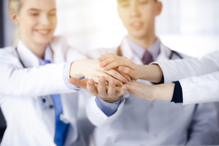 Group of doctors joining hands as a circle and ready to help patients while sitting at the desk in modern hospital office. Successful teamwork in medicine, Coronavirus countering conceptの写真素材