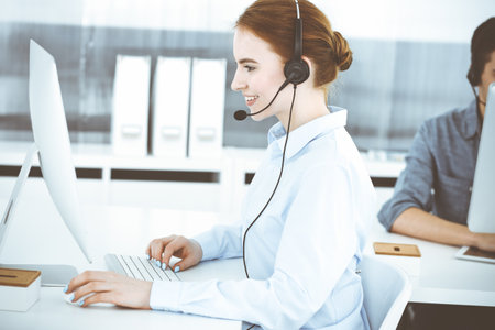 Young woman using headset and computer while talking with customers online. Group of Call center operators at work. Business conceptの写真素材