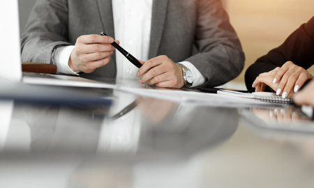 Unknown businessmen and woman sitting, using laptop computer and discussing questions at meeting in sunny office, close-up. Success conceptの写真素材