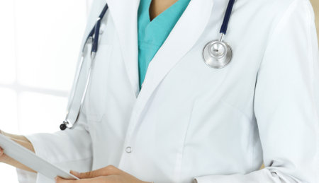 Unknown female doctor sitting and using tablet computer in clinic, close-up. Medicine conceptの写真素材