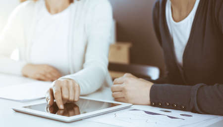 Businesswoman pointing at tablet computer screen while giving presentation to her female colleague. Group of business people working at the desk in office. Teamwork conceptの写真素材