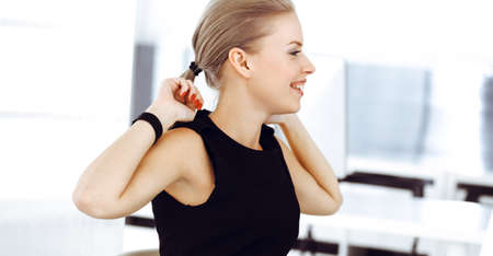 Young blond businesswoman working on computer while sitting at the desk in modern office. Business people concept. Secretary looks beautiful in black dressの写真素材