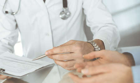 Unknown male doctor and woman-patient discussing current health examination while sitting in clinic and using clipboard. Good medical service in hospital. Medicine conceptの写真素材