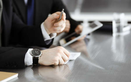 Unknown businessmen using tablet computer and work together at the glass desk in modern office,...