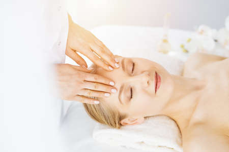 Beautiful caucasian woman enjoying facial massage with closed eyes in spa salon. Relaxing treatment in medicine and Beauty conceptの写真素材