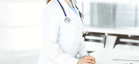 Unknown woman-doctor or internal student filling up medical documents while standing in clinic reception desk. Data in medicineの写真素材