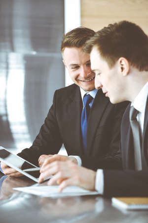 Businessman using tablet computer and work together with his colleague or partner at the glass desk in modern office. Unknown business people at meeting. Teamwork and partnership conceptの写真素材