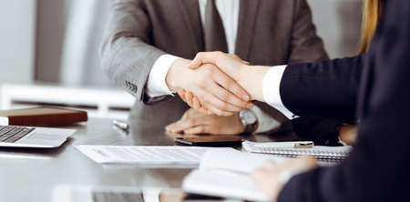 Unknown businessman shaking hands with his colleague or partner above the glass desk in modern office, close-up. Business people group at meetingの写真素材