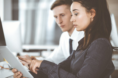 Business woman and man discussing questions while using tablet computer at workplace in modern office. Teamwork, meeting and brainstorming conceptの写真素材