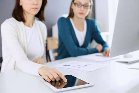 Businesswoman pointing at tablet computer screen while giving presentation to her female colleague. Group of business people working at the desk in office. Teamwork conceptの写真素材