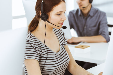 Casual dressed young woman using headset and computer while talking with customers online. Group of operators at work. Call center, business conceptの写真素材