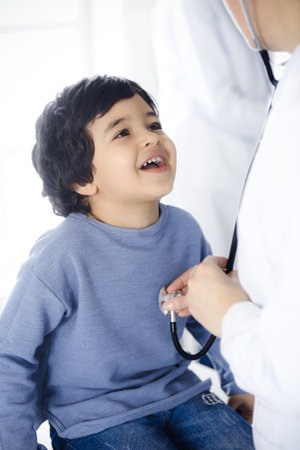 Doctor-woman examining a child patient by stethoscope. Cute arab boy at physician appointment. Medicine conceptの写真素材