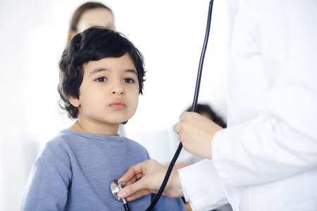 Doctor-woman examining a child patient by stethoscope. Cute arab boy and his brother at physician appointment. Medicine conceptの写真素材