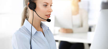 Blond woman working in sunny call center. Group of diverse people working as customer service occupation. Business conceptの写真素材