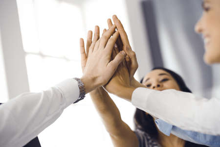 Group of business people joining hands or giving five to each other after meeting or negotiation in modern office. Colleagues showing teamwork, cooperation and partnership in corporate occupationの写真素材