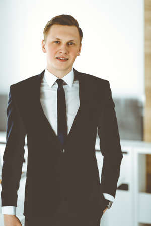 Cheerful businessman standing and looking at camera in office. Headshot of young and successful entrepreneurの写真素材