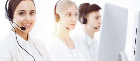 Call center in sunny office. Group of diverse operators at work. Beautiful woman in headset communicating with customers of telemarketing serviceの写真素材