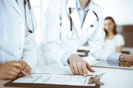 Unknown woman-doctors at work with patient at the background. Female physicians filling up medical...