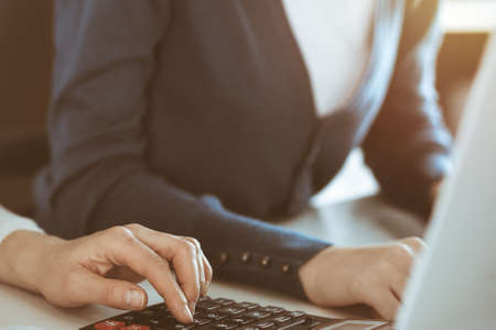 Accountant checking financial statement or counting by calculator income for tax form, hands closeup. Business woman sitting and working with colleague at the desk in office. Tax and Audit conceptの写真素材