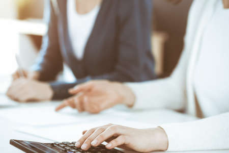 Accountant checking financial statement or counting by calculator income for tax form, hands closeup. Business woman sitting and working with colleague at the desk in office. Tax and Audit conceptの写真素材