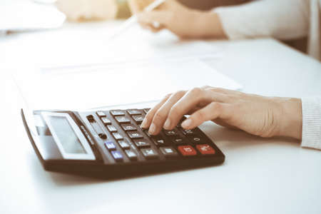 Accountant checking financial statement or counting by calculator income for tax form, hands closeup. Business woman sitting and working with colleague at the desk in office. Tax and Audit conceptの写真素材