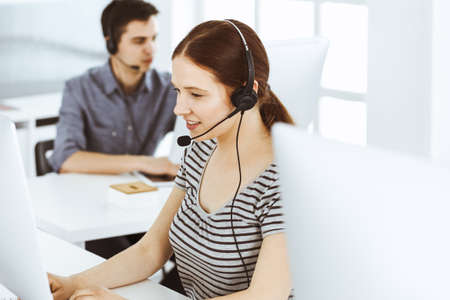 Casual dressed young woman using headset and computer while talking with customers online. Group of operators at work. Call center, business conceptの写真素材