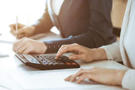 Accountant checking financial statement or counting by calculator income for tax form, hands closeup. Business woman sitting and working with colleague at the desk in office. Tax and Audit conceptの写真素材