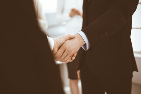 Businessman and woman shaking hands with colleagues at the background. Handshake at meeting in office. Concept of success in businessの写真素材