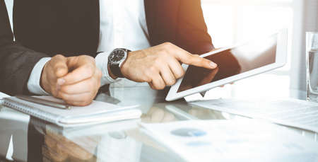 Business people using tablet computer while working together in sunny office. Unknown businessman sitting at the desk with his partnerの写真素材