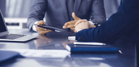 Unknown businessman using tablet computer and working together with his colleague while sits at the...