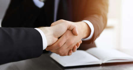 Businessman shaking hands with his colleague above the glass desk in sunny modern office, close-up. Unknown business people at meetingの写真素材