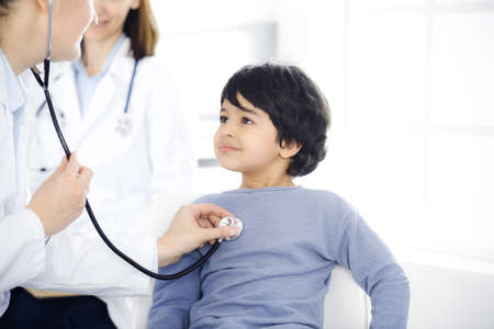 Doctor-woman examining a child patient by stethoscope. Cute arab boy at physician appointment....