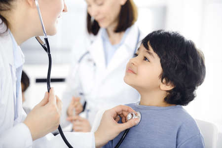 Doctor-woman examining a child patient by stethoscope. Cute arab boy at physician appointment. Medicine conceptの写真素材