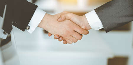 Unknown businessman shaking hands with his colleague or partner while standing straight in sunny...