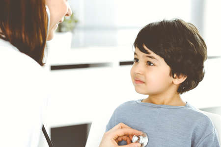 Doctor-woman examining a child patient by stethoscope. Cute arab boy at physician appointment....