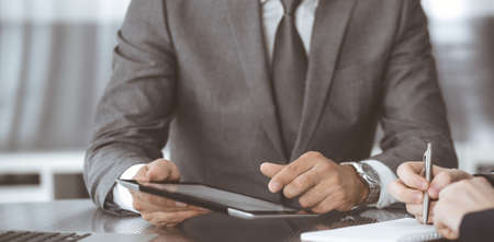Unknown businessman using tablet computer and working together with his colleague while sits at the...