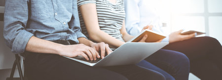 Group of casual dressed business people working at meeting or conference in sunny office, close-up of hands. Businessman using tablet computerの写真素材