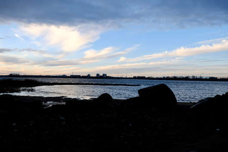 Empty coast of the river in autumn. Sunset time. Cloudy sky on background. Pink and blue colors of clouds. Dark shadows. dry reeds grow near the water. Selective focus.の写真素材