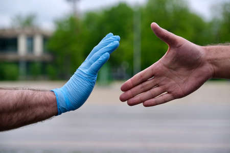 keep distance and safety to protect yourself from coronavirus. Man in rubber gloves stops the handshake of a man without protective gloves. Stop COVID-19の写真素材