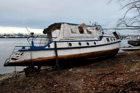 old broken ship moored on shallow near berth. Autumn season. Gray sky on backgroundの写真素材